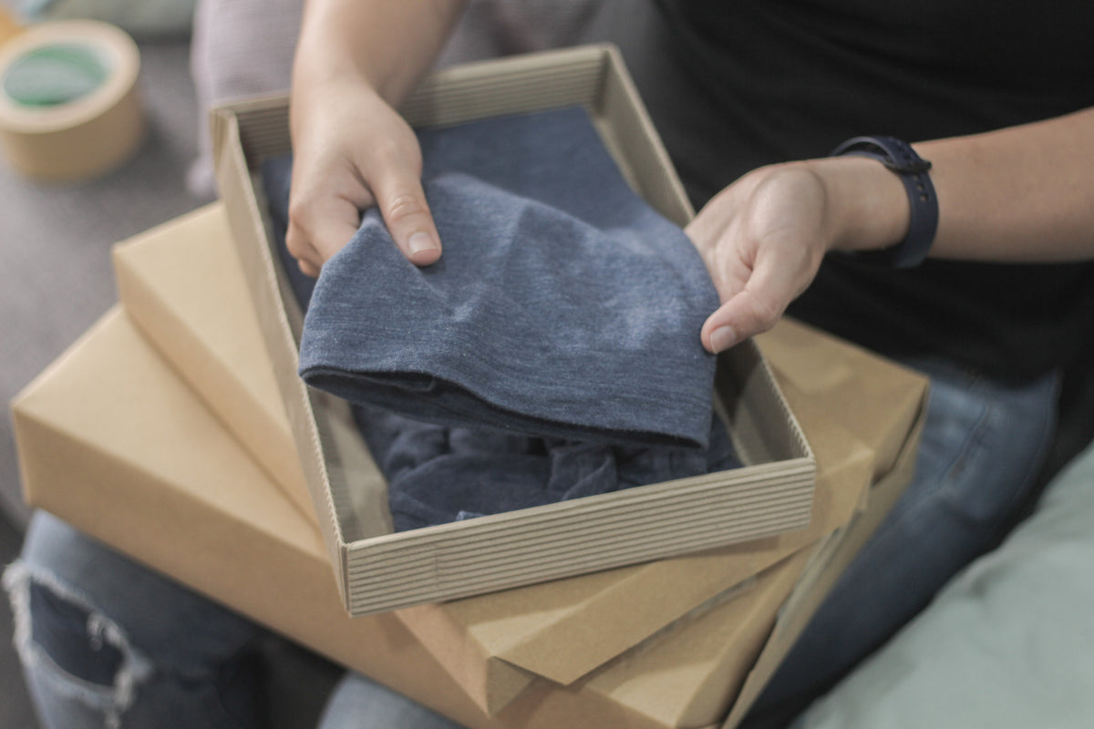 Person holding a folded blue garment in a cardboard box