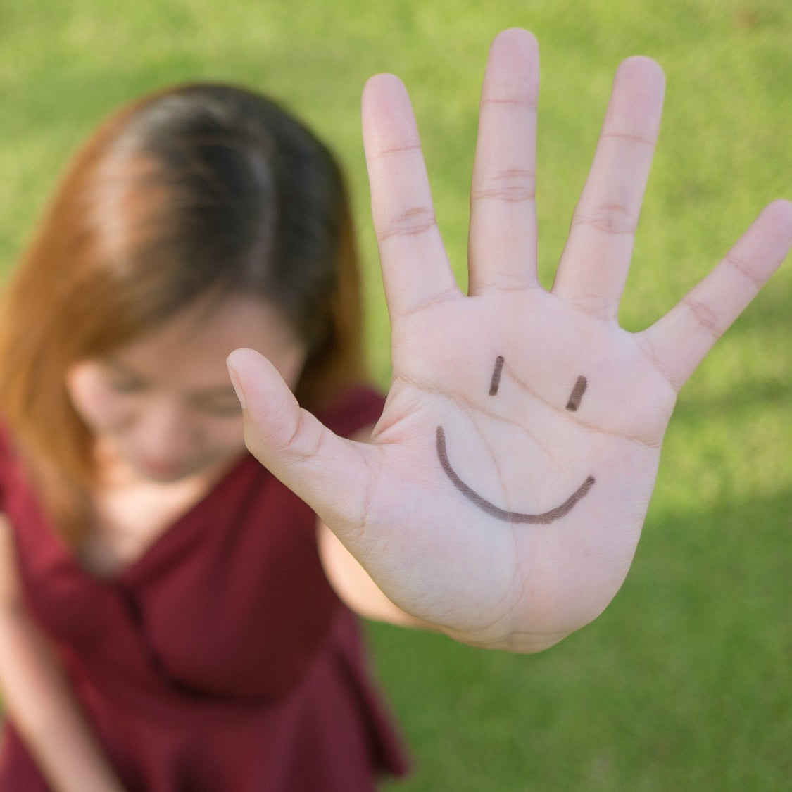 Person holding up a hand with a smiley face on a grassy background